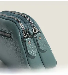 Macro shot of dual metal zippers and litchi grain cowhide leather on a teal handbag