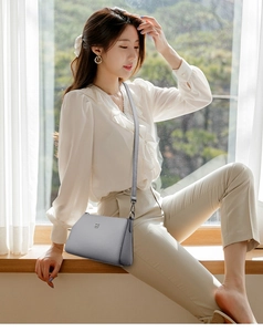 Detail of grey lychee leather texture and silver square metal logo on a crossbody bag