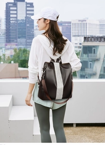 Rear view of a chic faux leather backpack in dark brown with a white stripe on a model