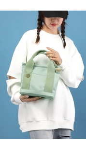 Detail of light green canvas tote bag with front pocket and round metal tag charm