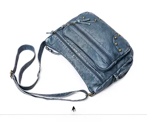 Detailed view of blue washed leather crossbody bag with multiple zippers and brass rivets