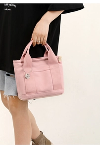 Detailed macro view of a pink canvas tote bag featuring a round metal logo pendant charm