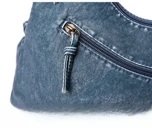 Close-up of a smooth gold metal zipper on a dark blue vintage leather shoulder bag