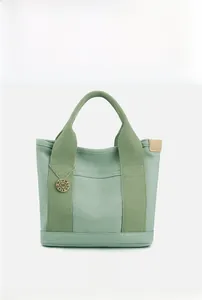 Close-up of green canvas tote bag featuring a vintage metal charm and side leather label