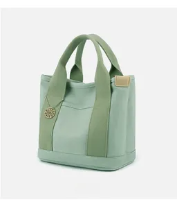 Detail view of the canvas handbag featuring olive green handles and a metallic logo tag