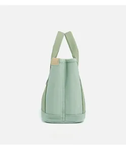 Detailed side view of light green canvas tote bag featuring premium leather label and stitching