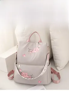 Close-up of light gray nylon backpack featuring pink cherry blossom embroidery and wide strap