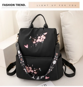 Close-up of pink cherry blossom embroidery on black nylon backpack with decorative strap
