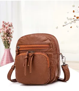 Detail of brown PU leather crossbody bag featuring multi-layer zippers and lychee texture