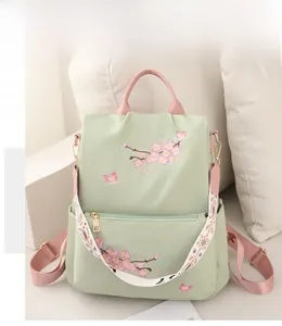 Detail of light green nylon backpack featuring cherry blossom embroidery and pink straps