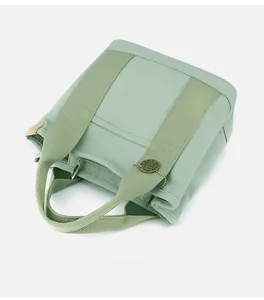 Detail of light green canvas tote bag showing top zipper and retro metal brand tag