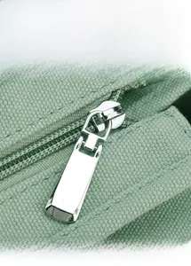 Close-up of smooth silver metal zipper and durable mint green canvas on a tote bag