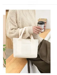 Detail of beige canvas tote bag with reinforced straps held by model in casual setting