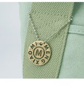 Detailed close-up of a vintage bronze M-logo metal pendant on a light green canvas handbag