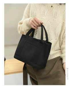 Close-up of black canvas handbag with reinforced handles and functional outer pocket