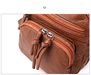 Detailed macro view of brown textured leather bag featuring dual metal zippers and knotted pulls