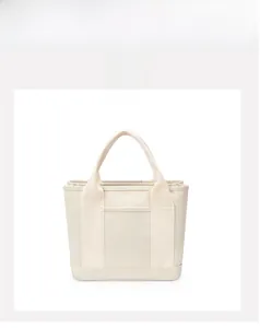 Front detail of beige canvas tote bag showing the functional outer pocket and dual handles
