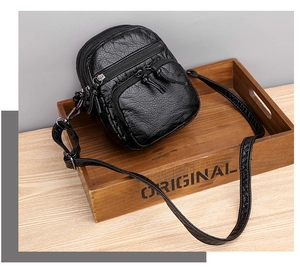 Detail of black PU leather crossbody bag featuring multiple zipper pockets and fringe tassels