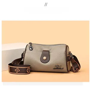 Détail d'un sac bandoulière taupe en cuir grainé avec logo et large sangle fleurie