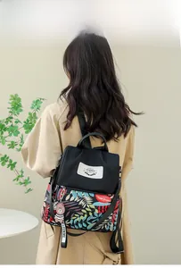 Rear view of model wearing a black floral print backpack with a cute bear charm