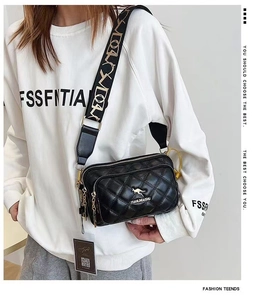 Detail view of black quilted crossbody bag with gold logo and multi-layer zippers