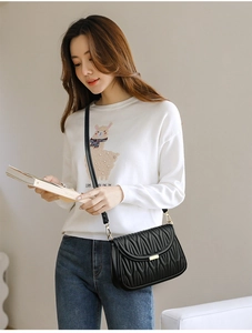 Detail of black matelassé crossbody bag featuring gold buckle and leather shoulder strap