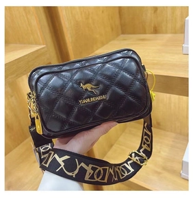Detail of black quilted crossbody bag with golden hardware and wide graphic strap