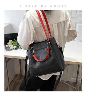 Detail of embossed letter pattern on black litchi leather tote with red handle accent