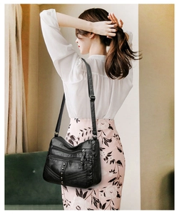 Detail of adjustable strap and side rivet accents on a soft black leather crossbody bag