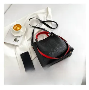 Detail of black embossed tote bag with red handles and gold rivets on a blazer