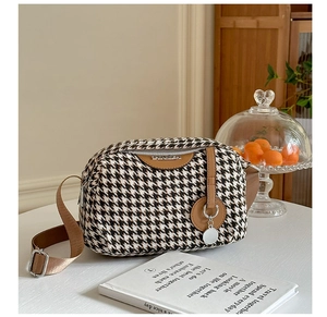 Detail of houndstooth canvas crossbody bag with brown leather trim and metal logo
