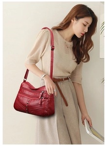 Detail of dark red crossbody bag showing multi-zipper pockets and rivet decor