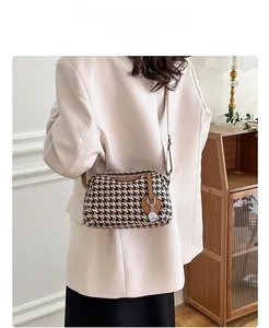 Model display of houndstooth shoulder bag with brown leather trim and metal pendant