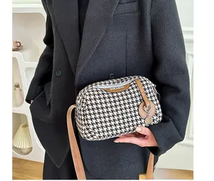 Detail of houndstooth crossbody bag with brown leather strap worn on black blazer
