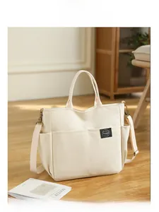 Détail du cabas en toile blanc cassé avec doubles poches avant et étiquette mode