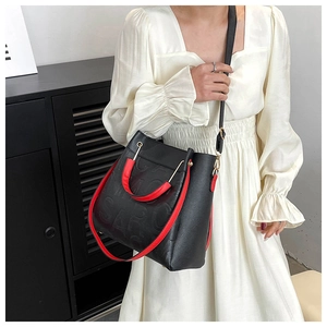 Detail of black embossed crossbody bag featuring vibrant red handles in a home setting