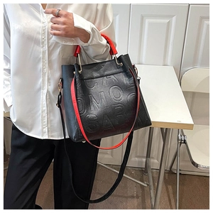 Detail of black pebbled leather handbag with embossed letters and red contrast handles