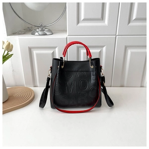 Detail of Boston bag featuring textured letter embossing and red top handles on black leather