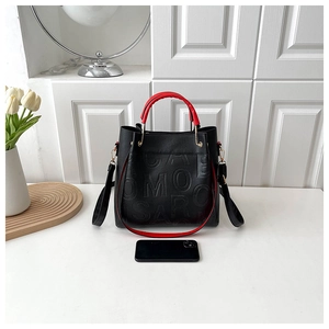 Detail of black pebbled leather tote with embossed letters and red contrast handles