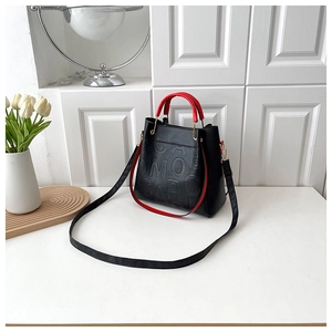 Detail of black pebbled leather tote bag with red handles and embossed lettering
