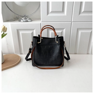 Detail of black pebbled leather tote with embossed letters and brown tubular handles
