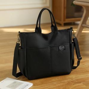 Sac cabas en toile noire avec bandoulière réglable et poches sur sol en bois clair