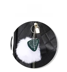 Close-up of a white fluffy ball pendant and green leaf charm on a black leather backpack