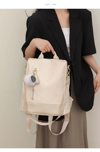 Detailed view of beige quilted faux leather backpack with plush ball charm on a model