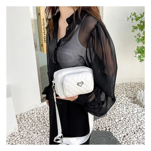 Detailed view of white quilted PU leather crossbody bag with dual zipper and heart ornament