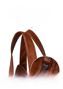 Detail of reinforced handles on brown pebble-grain leather bag with dark metal hardware