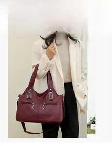 Detail view of burgundy leather shoulder bag with silver zippers shown on a model