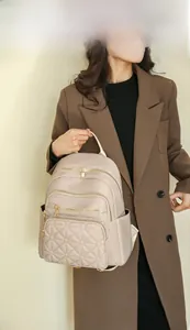Detail of beige quilted backpack with metal zippers held by a model in a brown coat