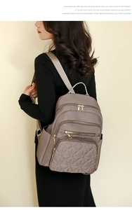 Detail view of mauve quilted backpack with gold zippers and side pockets on model