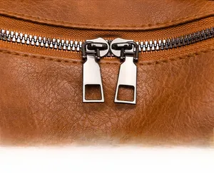 Detailed macro view of dual-way metal zippers on brown lychee-pattern leather backpack